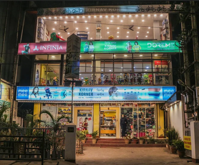 Exterior dusk photograph of Kirnav Korner illuminated three-floor children department store on RG Baruah Road Guwahati with customer parking
